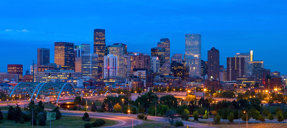Panorama of downtown Denver at dusk with a lit pedestrian bridge in the foreground