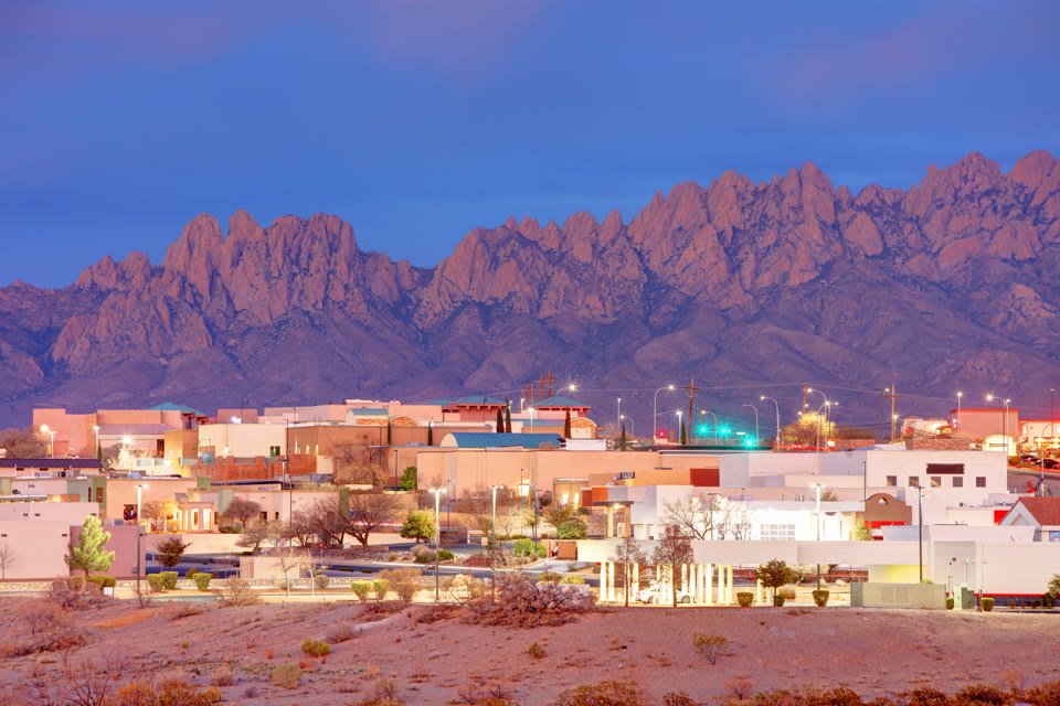 Adobe-style buildings lit up at dusk with the Organ Mountains silhouetted behind them in Las Cruces, New Mexico