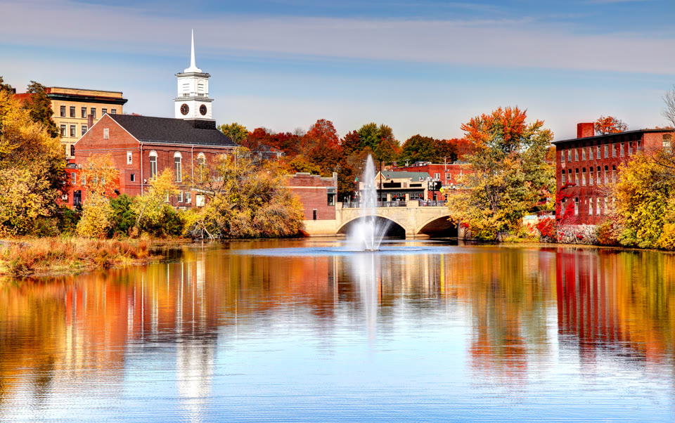 A fountain and bridge over the Nashua River with the historic mill and church in fall foliage in Nashua, New Hampshire