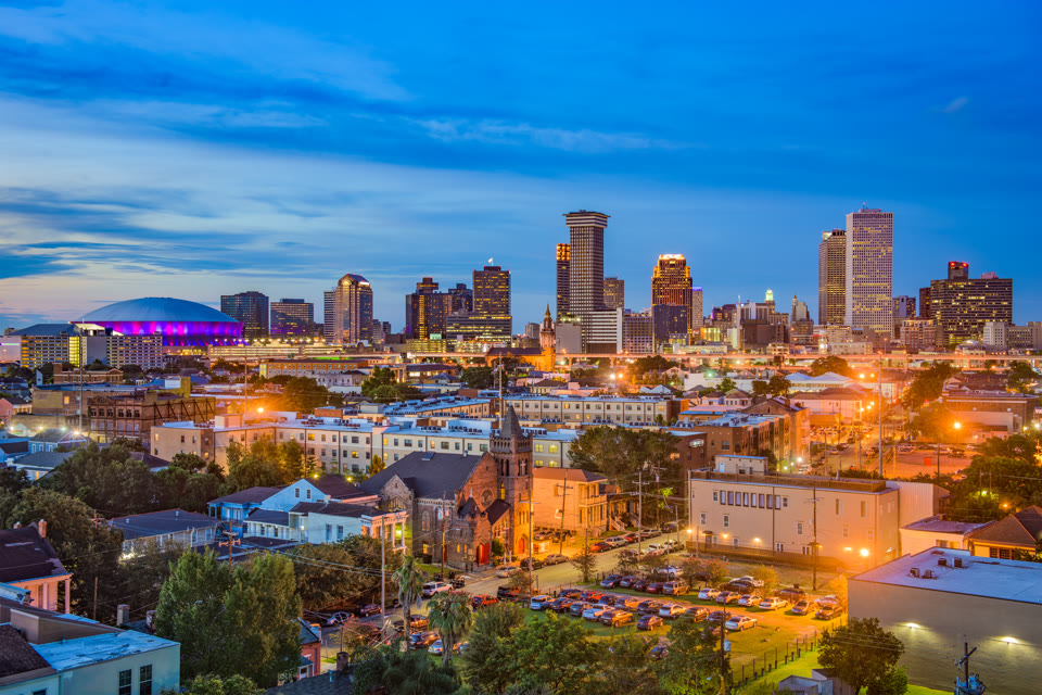 The Superdome lit up at blue hour beside the downtown New Orleans skyline